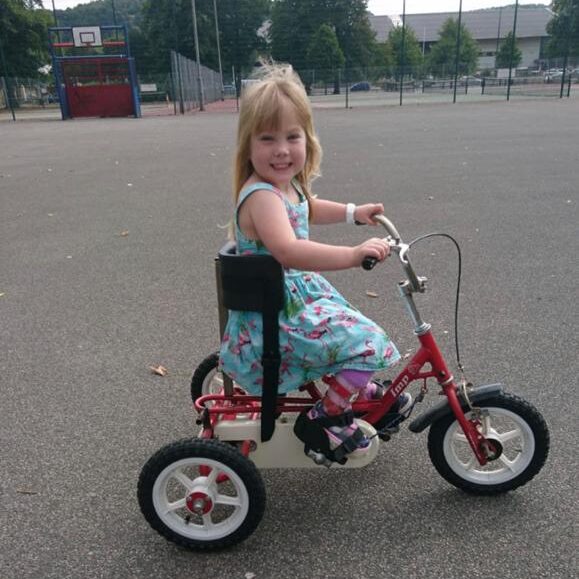A young girl, Edith, smiles while riding her second hand red trike.