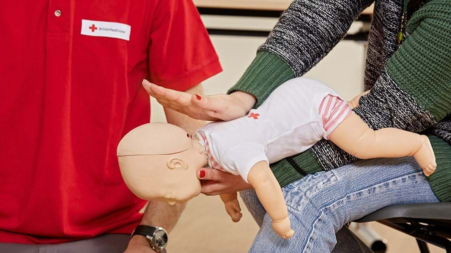 A person is participating in a first aid training course by practising saving a child from choking, using a doll.