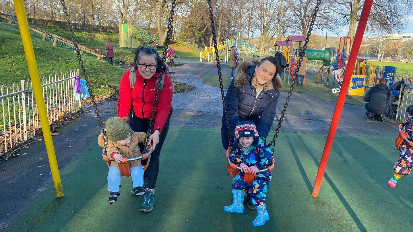 Two mums push their children who have spina bifida or hydrocephalus on the swings in a Sheffield park.