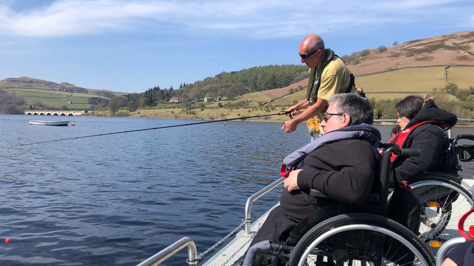 Two adults who are in wheelchairs are taking part in accessible fishing at Ladybower reservoir.