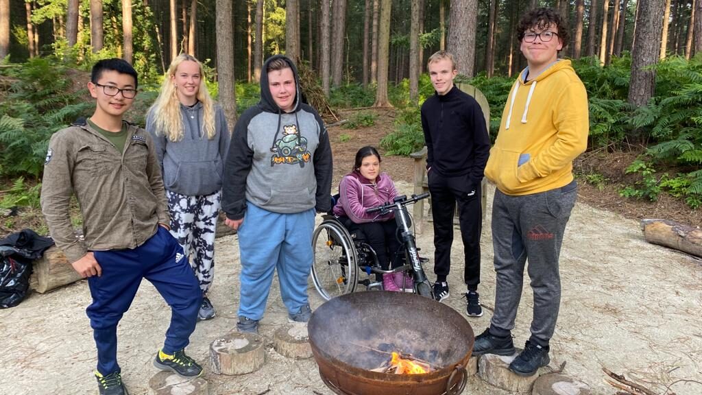Six teenagers smile for a photo around a firepit.