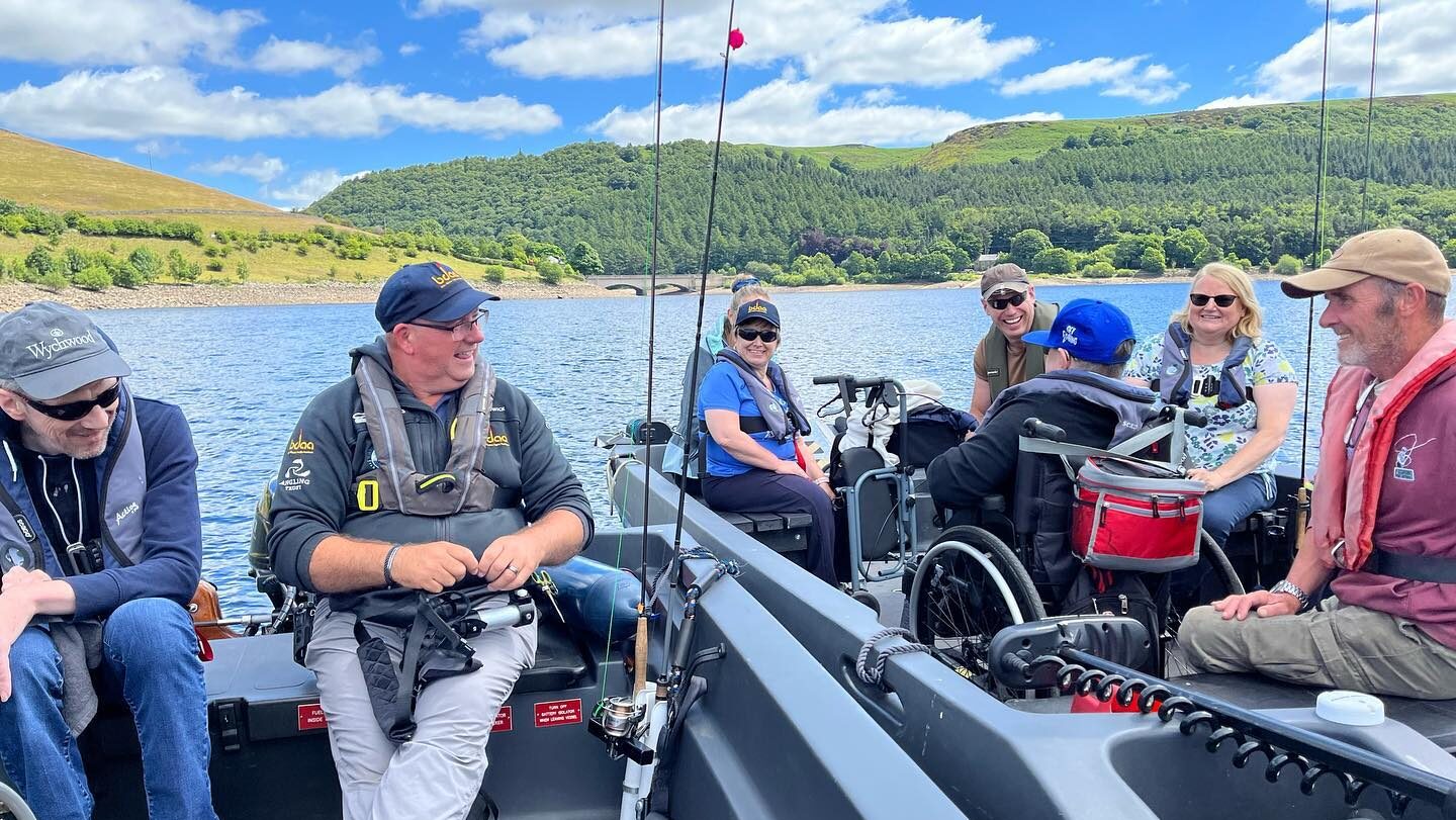 A group of people sit in an accessible fishing boat. They are out on the water at Ladybower Reservoir in the Peak District.